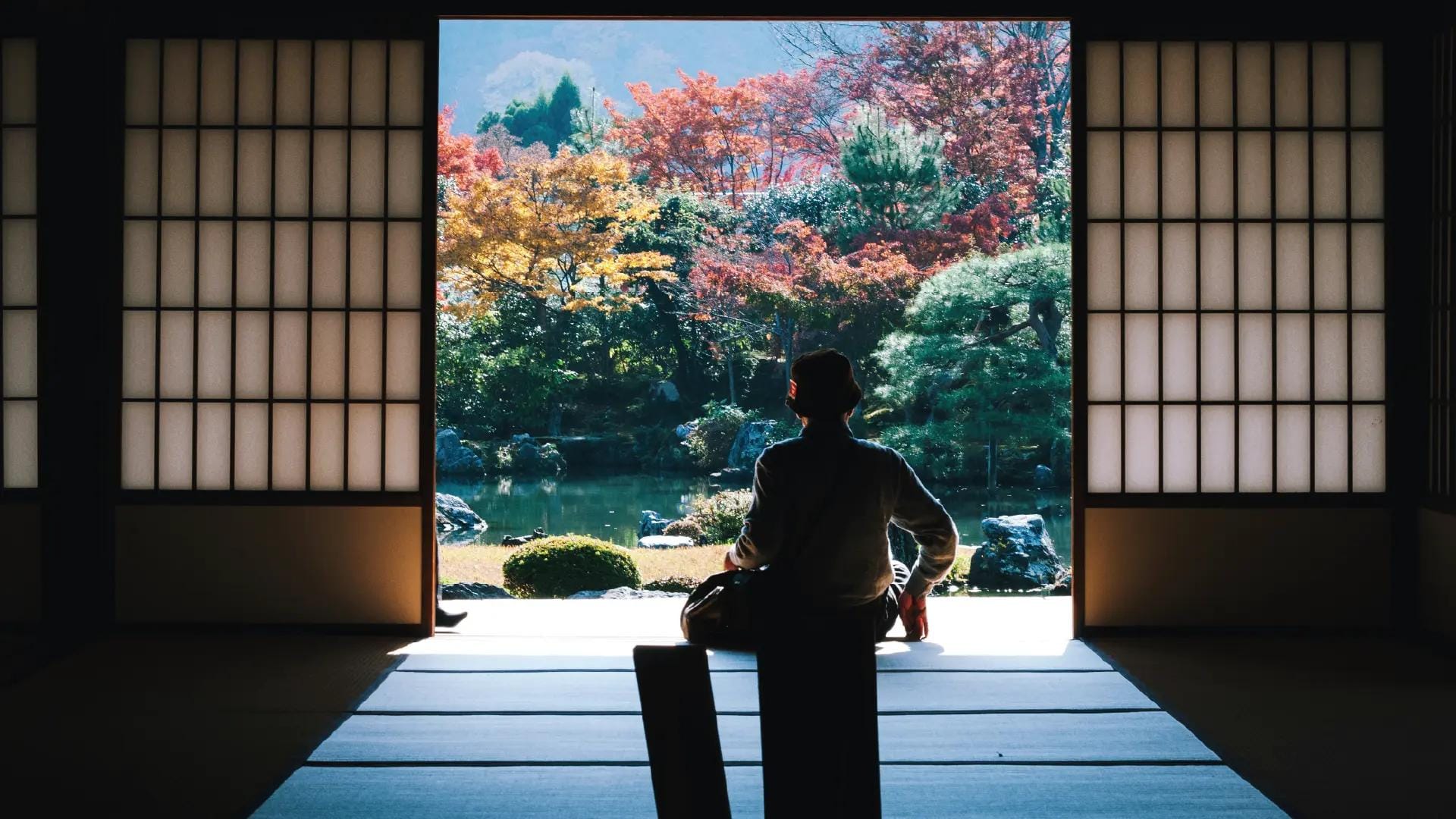 Persona seduta in una casa tradizionale giapponese che guarda un giardino autunnale.
