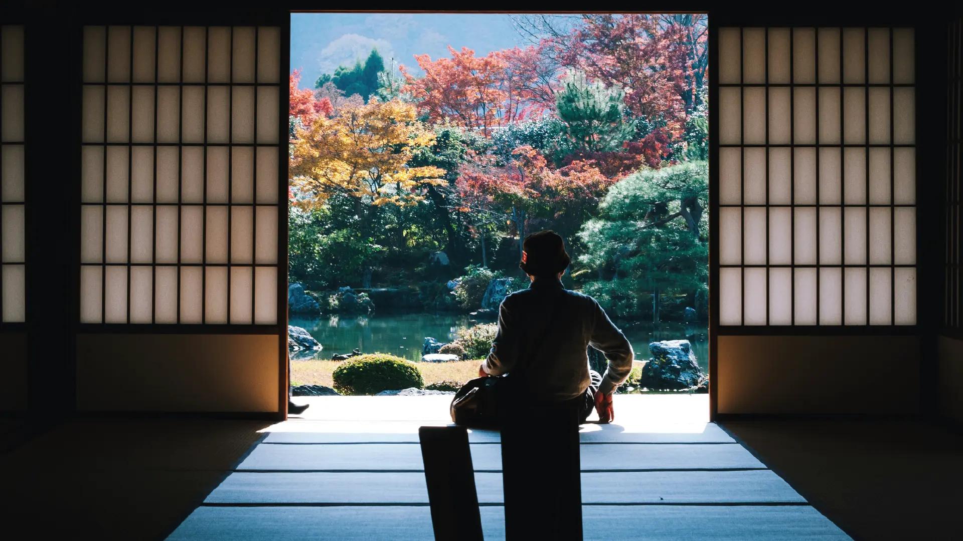 Persona seduta in una casa tradizionale giapponese che guarda un giardino autunnale.